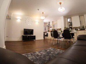 A modern living room with a flat-screen TV, a sofa, and a dining area with chairs. - Sav Rutland Town Centre-3 Bed Apartment (Leicester)