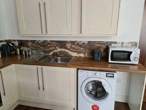 A compact kitchen with a washing machine, a microwave, and a sink. - Sav - Rutland, 4Bed in Leicester (Leicester)