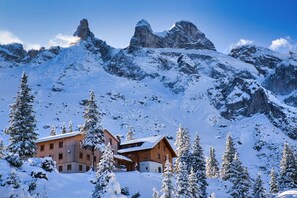 A mountain lodge with a wooden exterior, surrounded by snow-covered trees and rocky mountains. - Romanesque chalet with village view (Gaschurn)