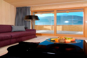 A modern living room with a red sofa, a glass coffee table with fruit, and a view of mountains through a sliding door. - Romanesque chalet with village view (Gaschurn)
