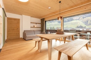 A modern interior with a wooden ceiling, a dining table with benches, a sofa, and a large window offering a view of a hilly landscape. - Holiday home in Neustift with swimming pool (Neustift)