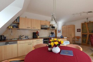 Une cuisine de taille réduite avec des meubles en bois, une table à manger recouverte d’une nappe rouge et un vase rempli de fleurs.