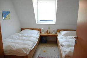 A small room with two single beds, a window, a wall-mounted light fixture, and a trash bin. - Holiday apartment with 2 bedrooms (Ostseebad Prerow)