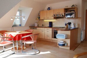 A compact kitchen with a dining area, featuring a table with chairs, wooden cabinets, and a microwave. - Holiday apartment with 2 bedrooms (Ostseebad Prerow)