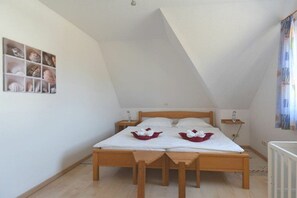 Un lit simple avec un cadre en bois et du linge de lit blanc, deux tables de chevet, une étagère murale agrémentée d’objets décoratifs et un plafond en pente.
