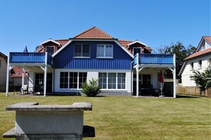 Une maison à deux étages, avec une façade bleue, un toit recouvert de tuiles rouges et une véranda couverte agrémentée d’un parasol rouge.
