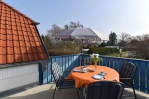 Un balcone con un tavolo apparecchiato per due persone, sedie e un ombrellone grande.