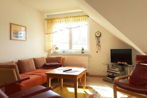 A cozy living room with a sofa, a table, a television, and a window with curtains. - Holiday apartment with 2 bedrooms (Ostseebad Prerow)