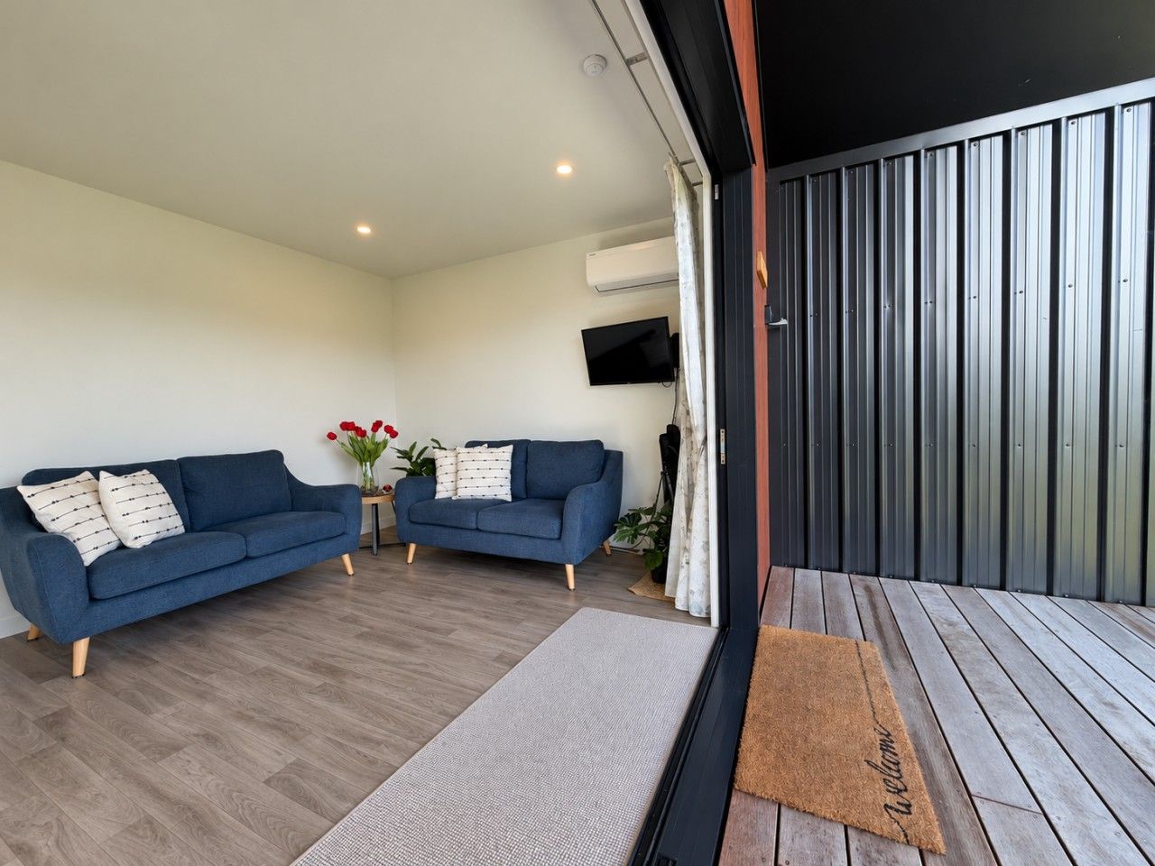 A modern living room with two sofas, a flat-screen TV, and a wooden deck.