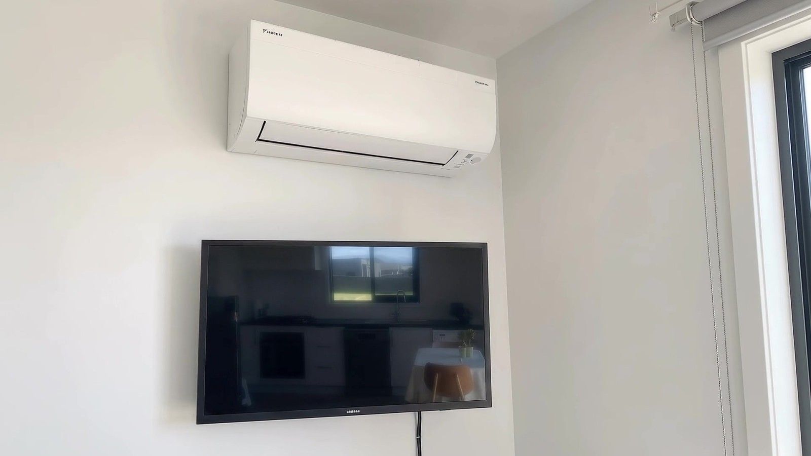 A flat-screen TV mounted on a wall with a white air conditioning unit above it.
