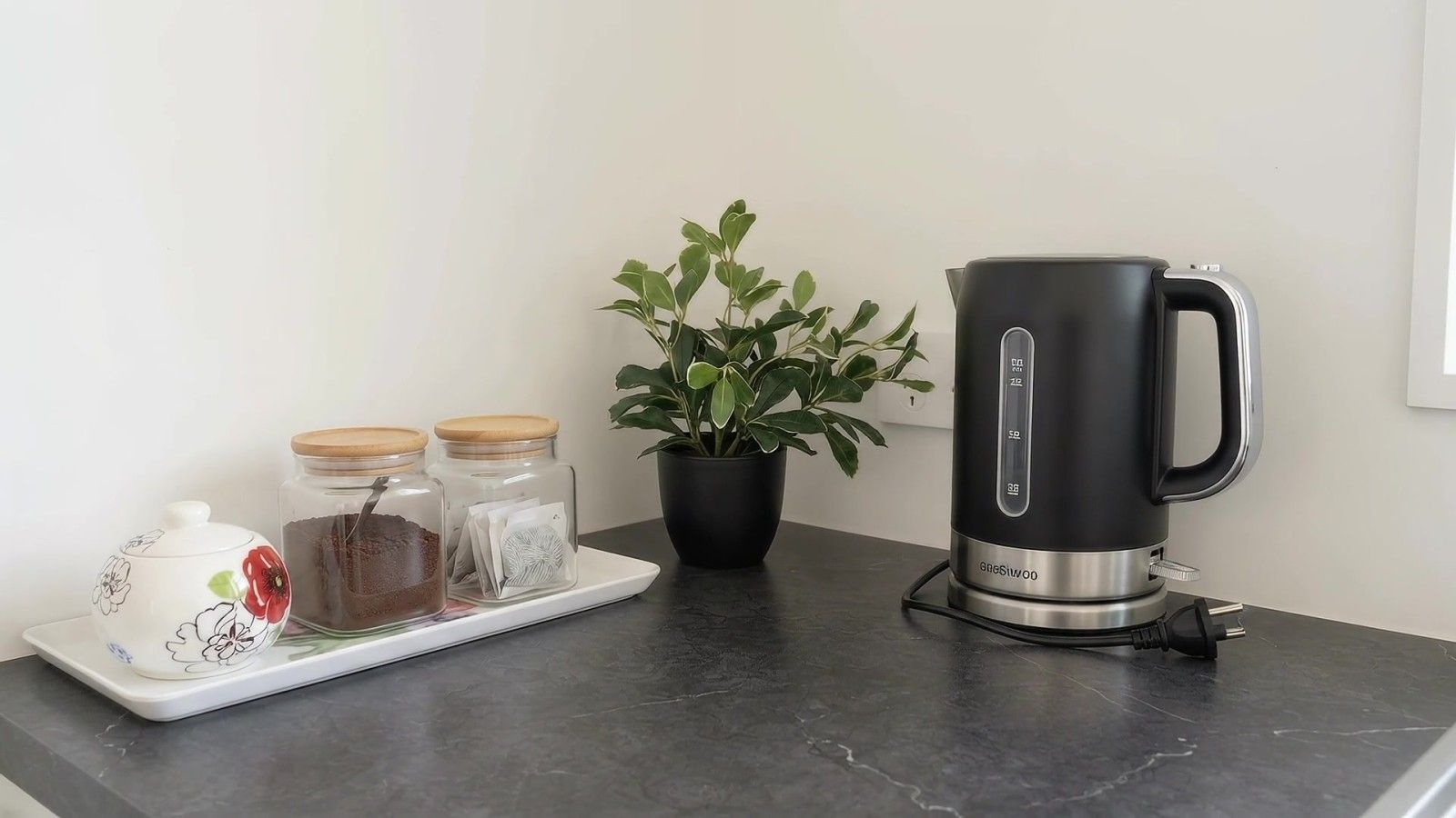 A kitchen counter with a black electric kettle, a white teapot, and two glass jars with lids.