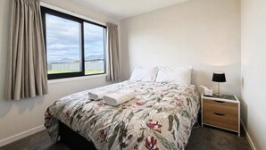 Quarto de hotel com uma cama grande, mesa de cabeceira, luminária e janela com cortinas.