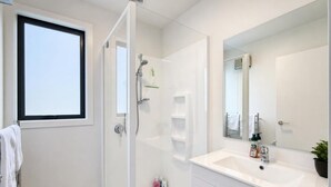 Casa de banho moderna com cabine de duche em vidro, toucador branco com um espelho grande e janela que proporciona luz natural.