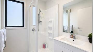 A modern bathroom with a glass shower enclosure, a white vanity with a large mirror, and a window providing natural light.