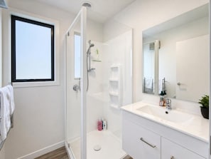 A modern bathroom with a glass shower enclosure, a white vanity with a large mirror, and a window providing natural light. - Glaisnock Cottage Te Anau (Te Anau)