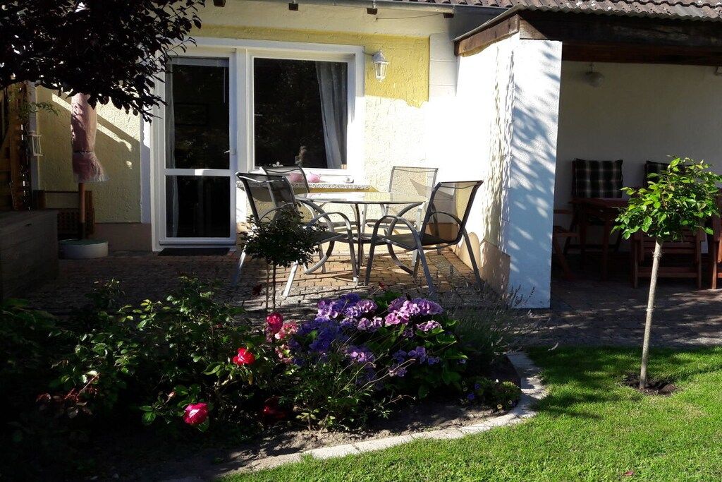 Eine Terrasse mit Tisch und Stühlen, ein kleiner Garten mit Blumen und ein Gebäude mit gelber Fassade.