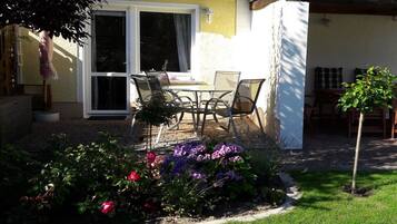 Eine Terrasse mit Tisch und Stühlen, ein kleiner Garten mit Blumen und ein Gebäude mit gelber Fassade.
