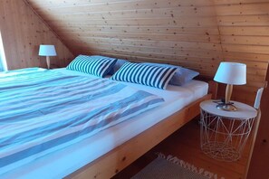 Ein Schlafzimmer einer Holzhütte mit einem Bett, zwei Nachttischlampen und einem runden Tisch mit Drahtgestell.