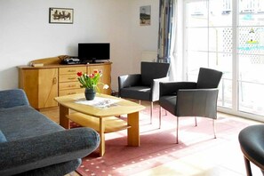 A living room with a sofa, a coffee table, a TV on a wooden cabinet, and a chair. - At the Stems W 1 || Prerow (Prerow)