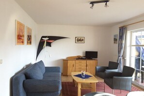 A living room with a sofa, a table with a bottle, and a TV on a wooden cabinet. - At the Stems W 1 || Prerow (Prerow)