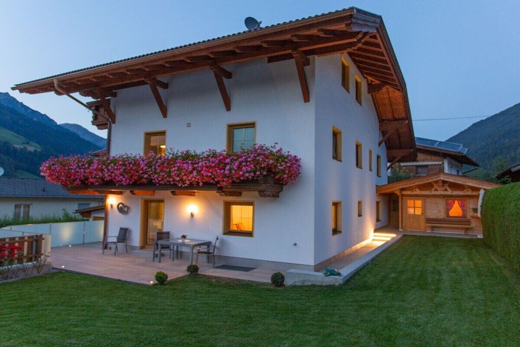 Une maison à deux étages avec un balcon, une terrasse dotée de mobilier d’extérieur et une vue sur les montagnes.