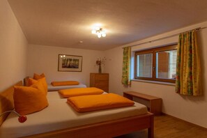 Une chambre à coucher comprenant un lit, deux oreillers, une table de chevet, une commode, une fenêtre avec des rideaux, un luminaire fixé au mur et un tableau encadré.