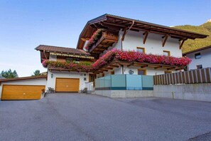 A two-story building with a balcony adorned with flowers, a garage, and a clear sky. - Holiday apartment with 2 bedrooms (Neustift im Stuibaital)