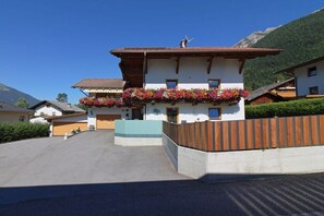 Ein zweistöckiges Gebäude mit einem Blumen geschmückten Balkon, einem Holzzaun und einem Berg im Hintergrund.