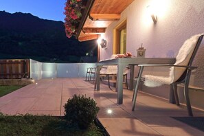 Une terrasse extérieure avec une table et des chaises, un petit jardin et une vue sur les montagnes en arrière-plan.