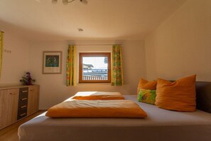 Ein Schlafzimmer mit einem Bett, einem Fenster, Vorhängen, einem Nachttisch und einem Bild an der Wand.
