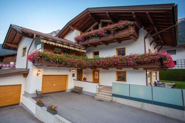 Un chalet à deux étages doté d’un balcon en bois, d’une entrée principale et d’un garage apparent.