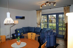 A dining area with a round table, chairs, a potted plant, and a blue sofa. - Oak Park W 2.2 || Ostseebad Prerow (Ostseebad Prerow)