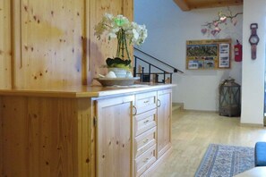 Ein Holzkabinent mit Schubladen, eine Vase mit weißen Blumen, eine kleine Schale mit Eiern und eine Wand mit einem Feuerlöscher und einer Uhr.