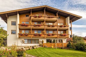 A multi-story building with balconies, a wooden facade, and a well-maintained garden. - at the Zedlacherhof guesthouse (Matrie in Osttirol)