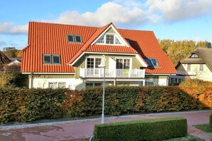 Een woonhuis met twee verdiepingen, een rood dak, witte details en een balkon.