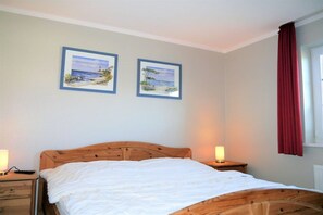 Ein Schlafzimmer mit einem hölzernen Bett, zwei Nachttischen und zwei gerahmten Bildern an der Wand.
