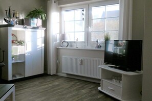 A room with a white cabinet, a television on a stand, a window with curtains, and a radiator. - Holiday apartment with 2 bedrooms (Ostseebad Prerow)