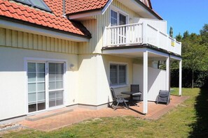 Ein zweistöckiges Haus mit überdachter Terrasse, einem Balkon und einer Statue auf dem Dach.