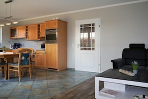 Eine kompakte Küche mit Holzausstattung, ein Essbereich mit Tisch und Stühlen sowie ein Wohnbereich mit einer schwarzen Couch.