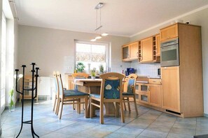 Een moderne keuken met houten kastjes, een inbouwoven en een eethoek met stoelen en een tafel.