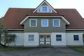 A two-story building with a gabled roof, a front door with decorative glass panels, and a brick driveway. - Holiday apartment with 2 bedrooms (Ostseebad Prerow)