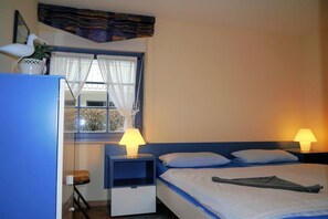 A hotel room with a bed, two bedside lamps, a nightstand, a window with curtains, and a small table with a chair. - Oak Park W 2.1 || Ostseebad Prerow (Ostseebad Prerow)