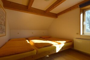 Ein Zimmer mit schrägem Dach, Holzbalken, einem Fenster und einem Bett mit orangefarbener Bettwäsche.
