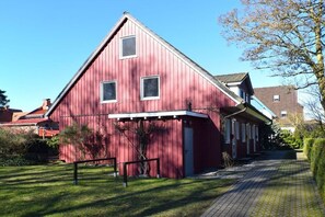 Ein rotes Bauernhaus mit Satteldach, einer gepflasterten Auffahrt und einem kleinen Baum im Vordergrund.