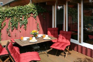 Eine Holzterrasse mit einem für zwei Personen gedeckten Tisch, umgeben von roten Sitzgelegenheiten mit Kissen.