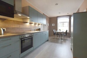 A modern kitchen with grey cabinets, a built-in oven, and a dining area with a table and chairs. - Captain's House W 6.23 (Ostseebad Prerow)