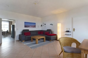 A living room with a sofa, a coffee table, a wicker chair, and a dining table. - Captain's House W 6.23 (Ostseebad Prerow)