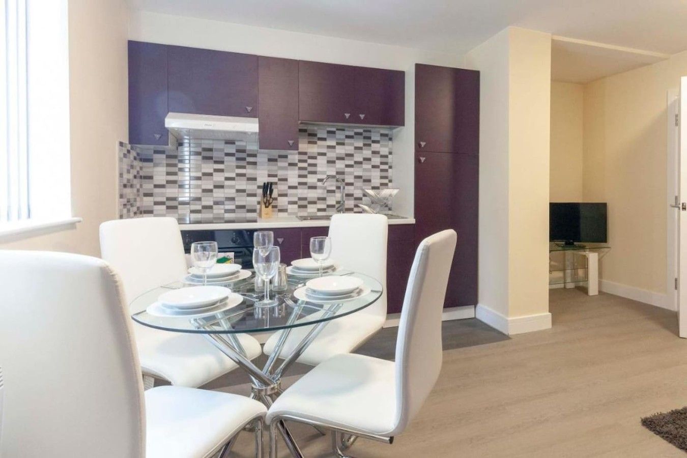 A modern kitchen with purple cabinets, a glass dining table, and white chairs.