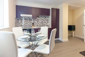 A modern kitchen with purple cabinets, a glass dining table, and white chairs. - SAV Clarence Apt, Loughborough - 2-Bed Ladybird (Leicestershire)