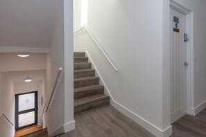 A staircase with a handrail leading to a door with a sign. - SAV Clarence Apt, Loughborough - 2-Bed Ladybird (Leicestershire)